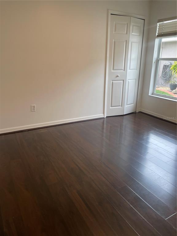 An empty room with dark wood flooring, white walls, a closet, and a window — 5418 FREDERICK LAKE DRIVE, PORT ORANGE, FL