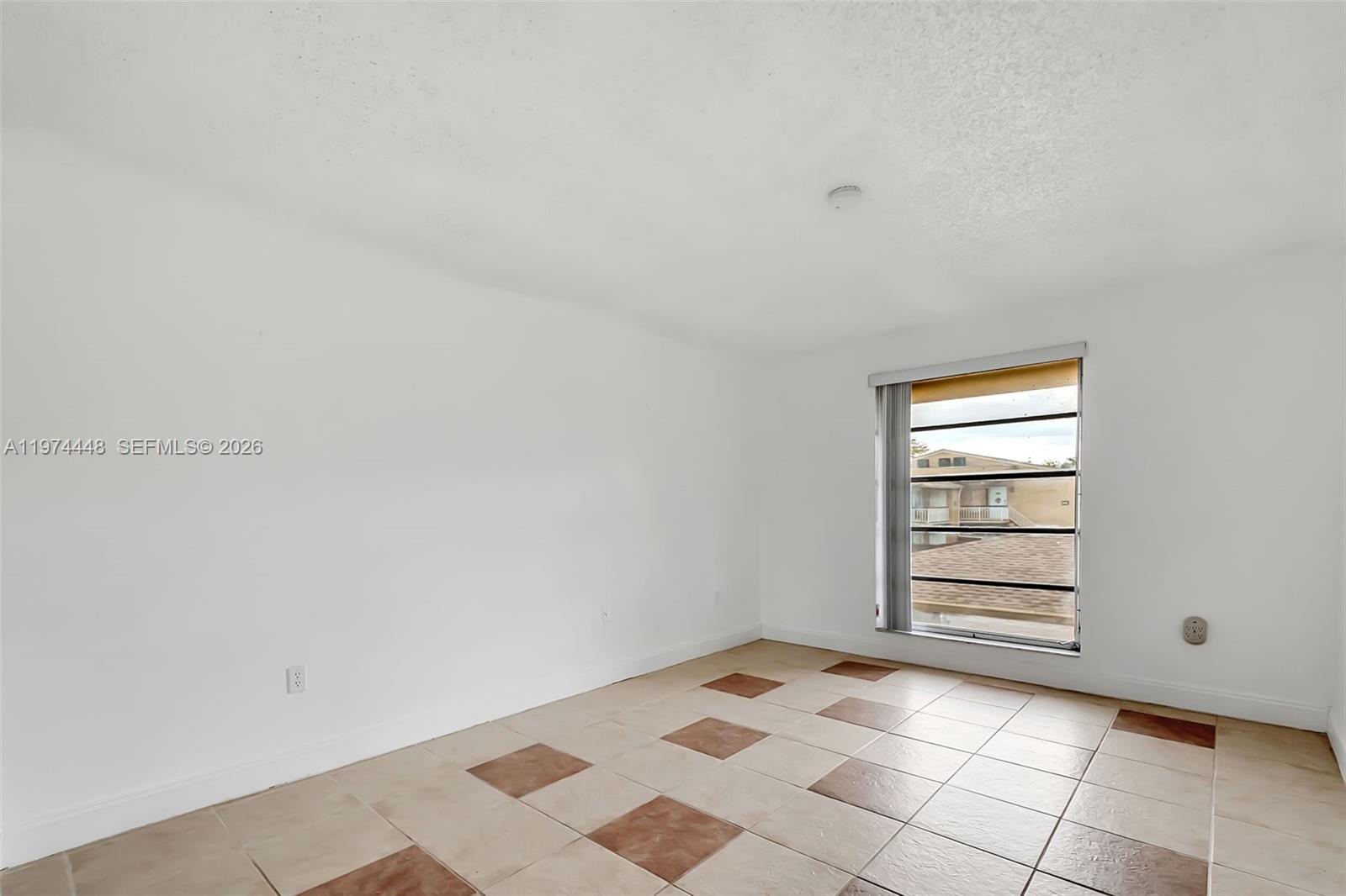 An empty room features white walls, tiled flooring with brown accents, and a single window — 13787 SW 66th St # 254D, Miami FL 33183, MIAMI, FL