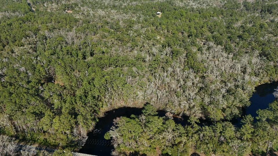 An aerial view shows a wooded lot bordering a winding creek near a paved road — 0 CHEROKEE DRIVE, SOPCHOPPY, FL