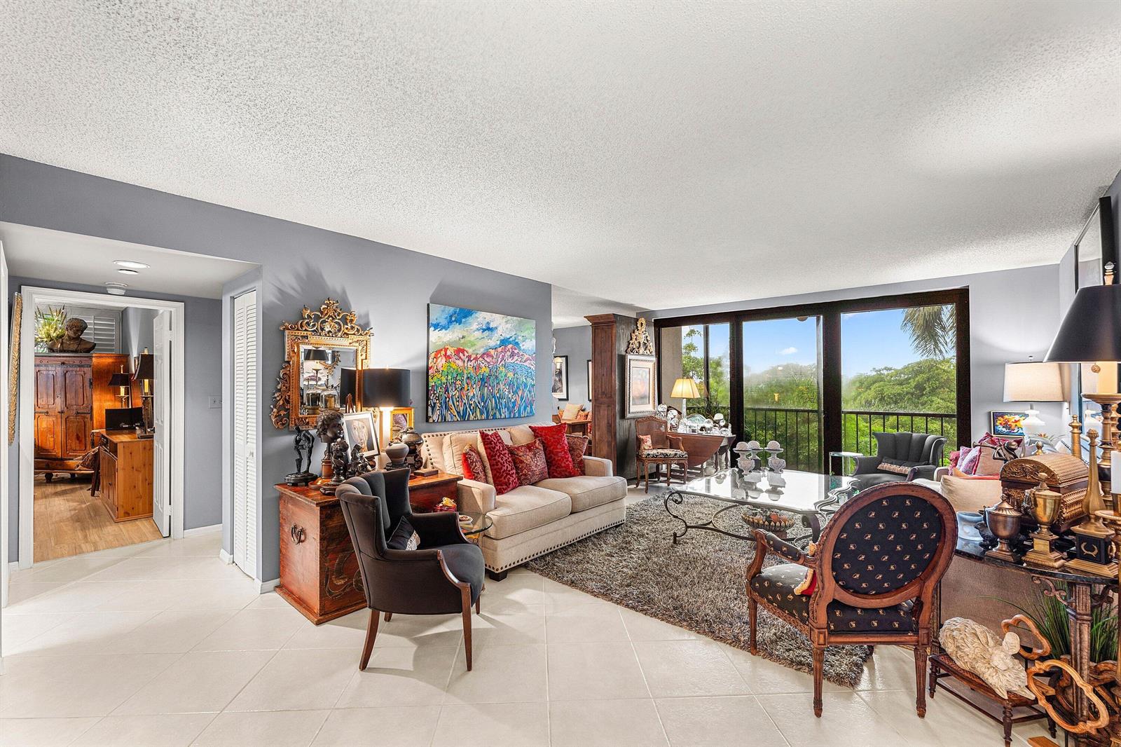 A living room features a beige sofa, patterned armchairs, a glass coffee table, and balcony views — 5951 Wellesley Park Drive # 507, Boca Raton FL 33433, BOCA RATON, FL