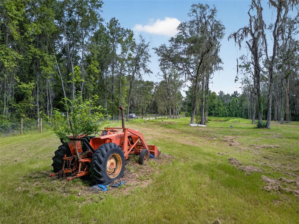 An orange tractor sits in a grassy field surrounded by trees under a blue sky — 16545 NW 128TH TERRACE Lot 37 & 36, REDDICK, FL