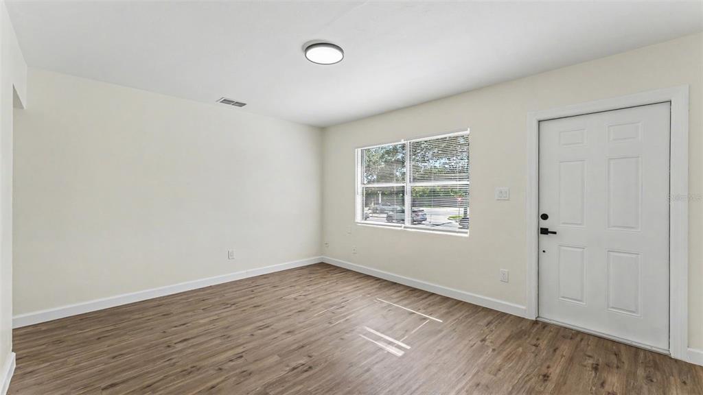 An empty room features light-colored walls, wood-look flooring, a window, and a white door — 621 HOLLINGSWORTH ROAD, LAKELAND, FL