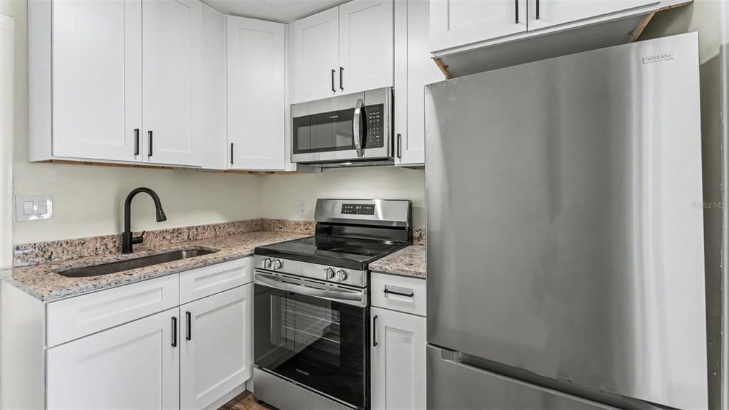 A kitchen features white cabinets, granite countertops, and stainless steel appliances — 621 HOLLINGSWORTH ROAD, LAKELAND, FL
