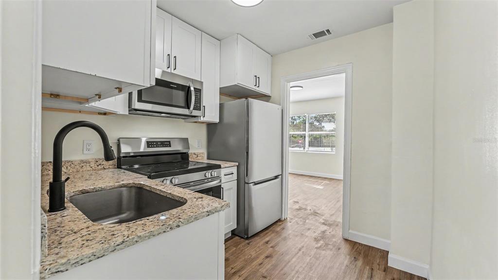 A kitchen features white cabinets, granite countertops, stainless steel appliances, and wood-look flooring — 621 HOLLINGSWORTH ROAD, LAKELAND, FL