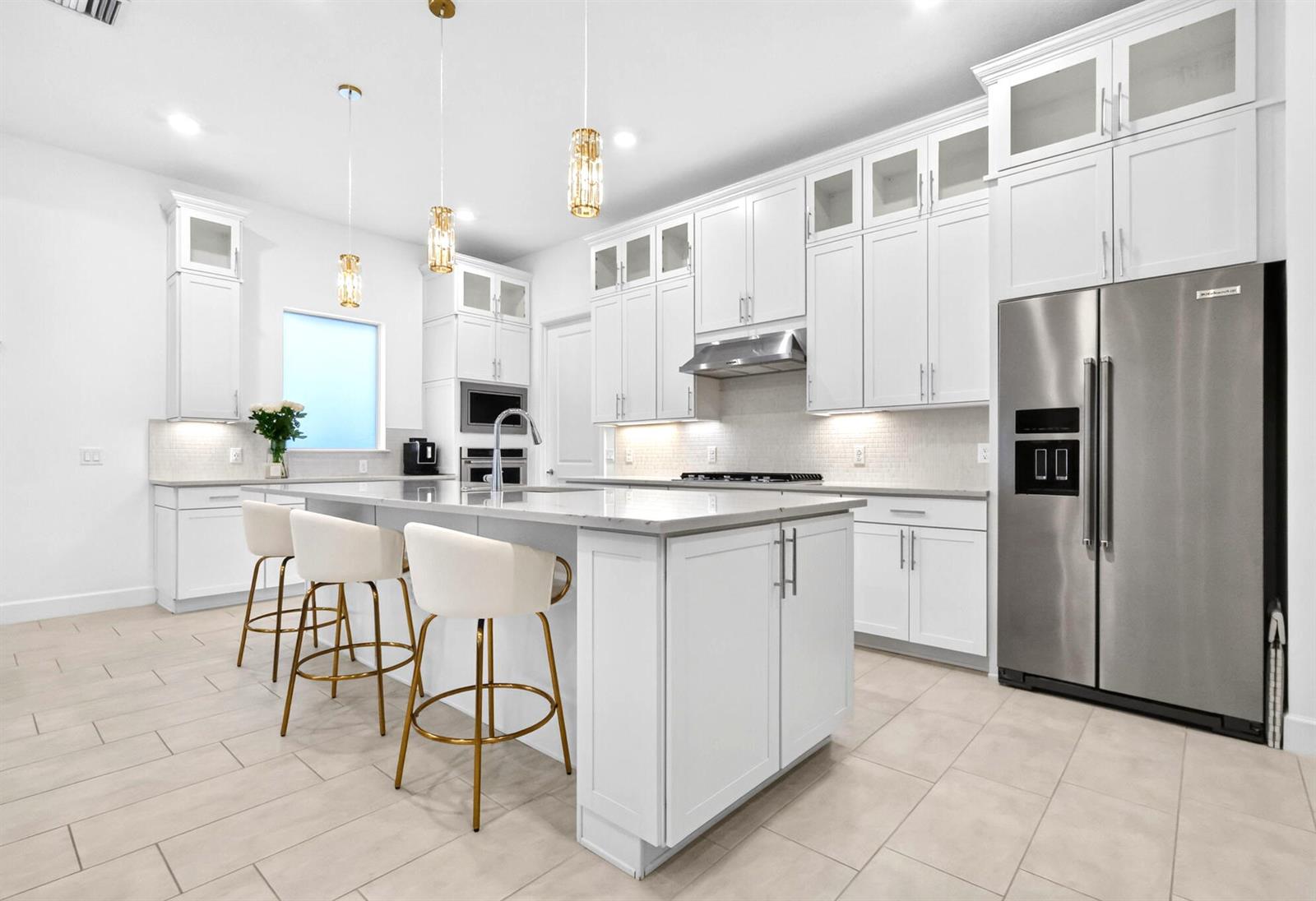 A modern kitchen features white cabinetry, a large island with bar stools, and stainless appliances — 4336 Matilda Court, Delray Beach FL 33445, DELRAY BEACH, FL
