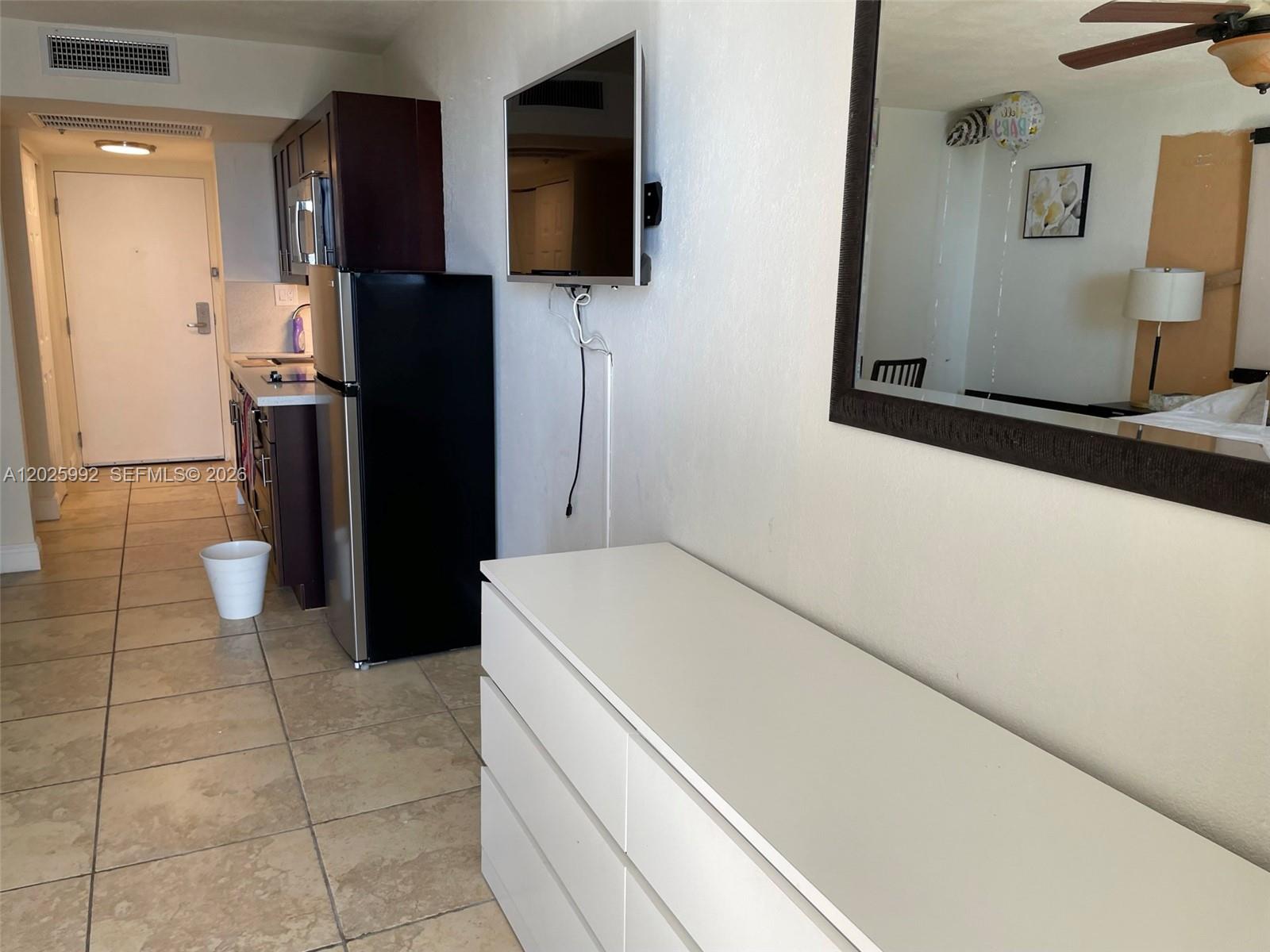 A white dresser sits in a room with a wall-mounted television and kitchen area — SUNNY ISLES BEACH, FL