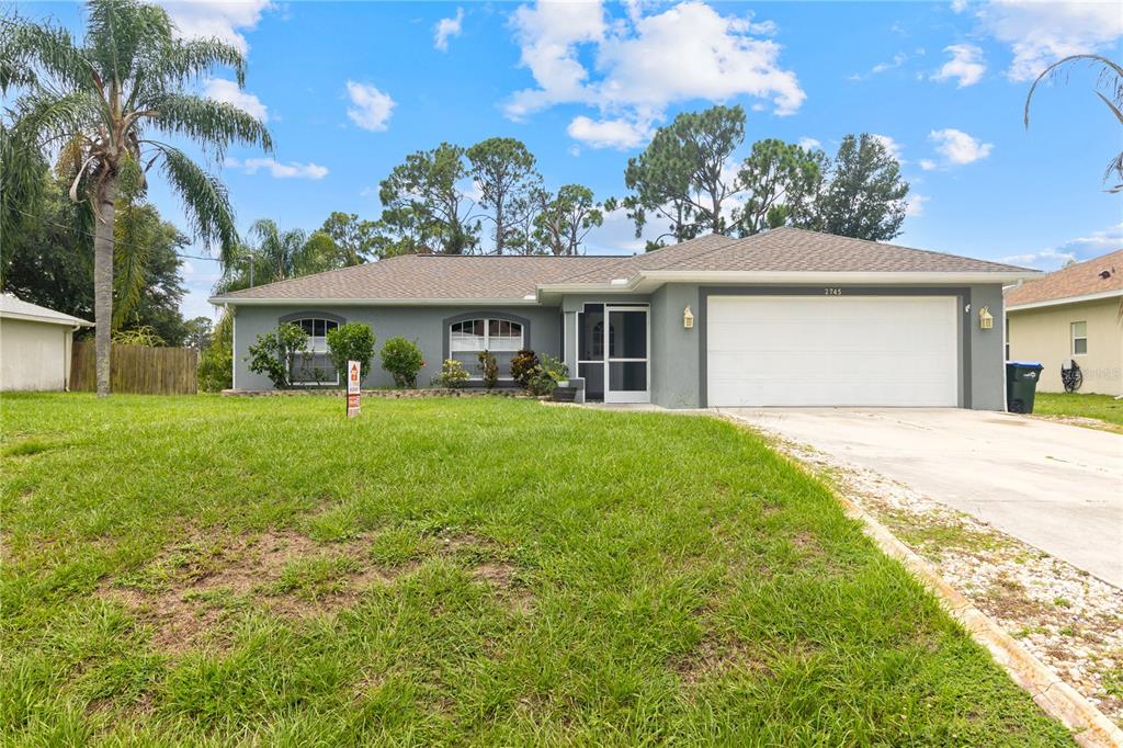 A single-story gray house with a two-car garage and a front lawn under a blue sky — 2745 NELLIE LANE, NORTH PORT, FL