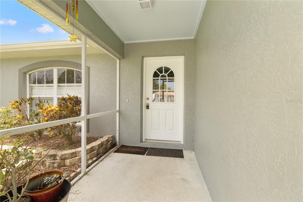A white front door with a glass insert sits on a covered concrete porch — 2745 NELLIE LANE, NORTH PORT, FL