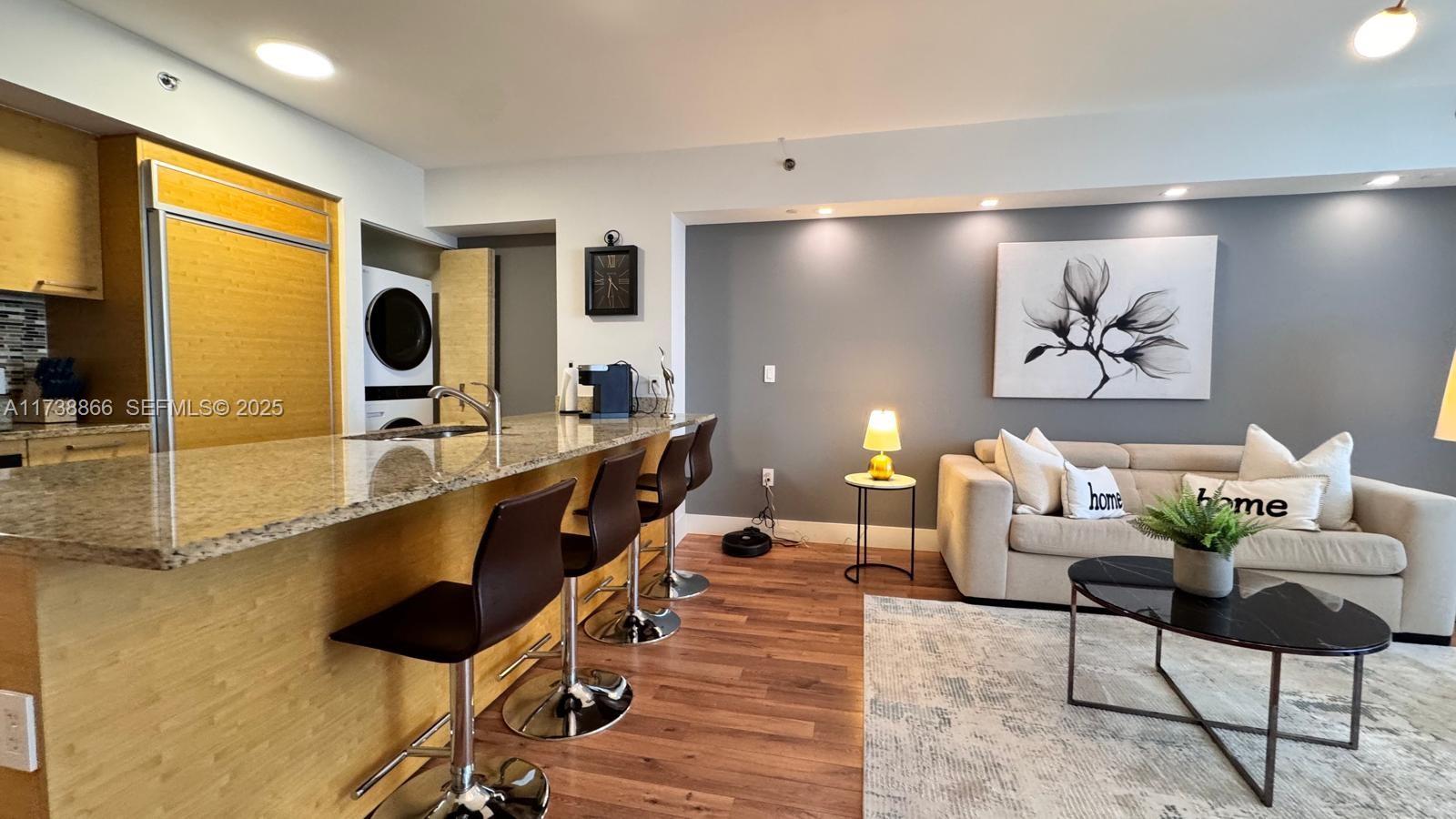 A kitchen with a granite breakfast bar and stools opens into a living room area — 1830 S Ocean Dr # 2209, Hallandale Beach FL 33009, HALLANDALE BEACH, FL