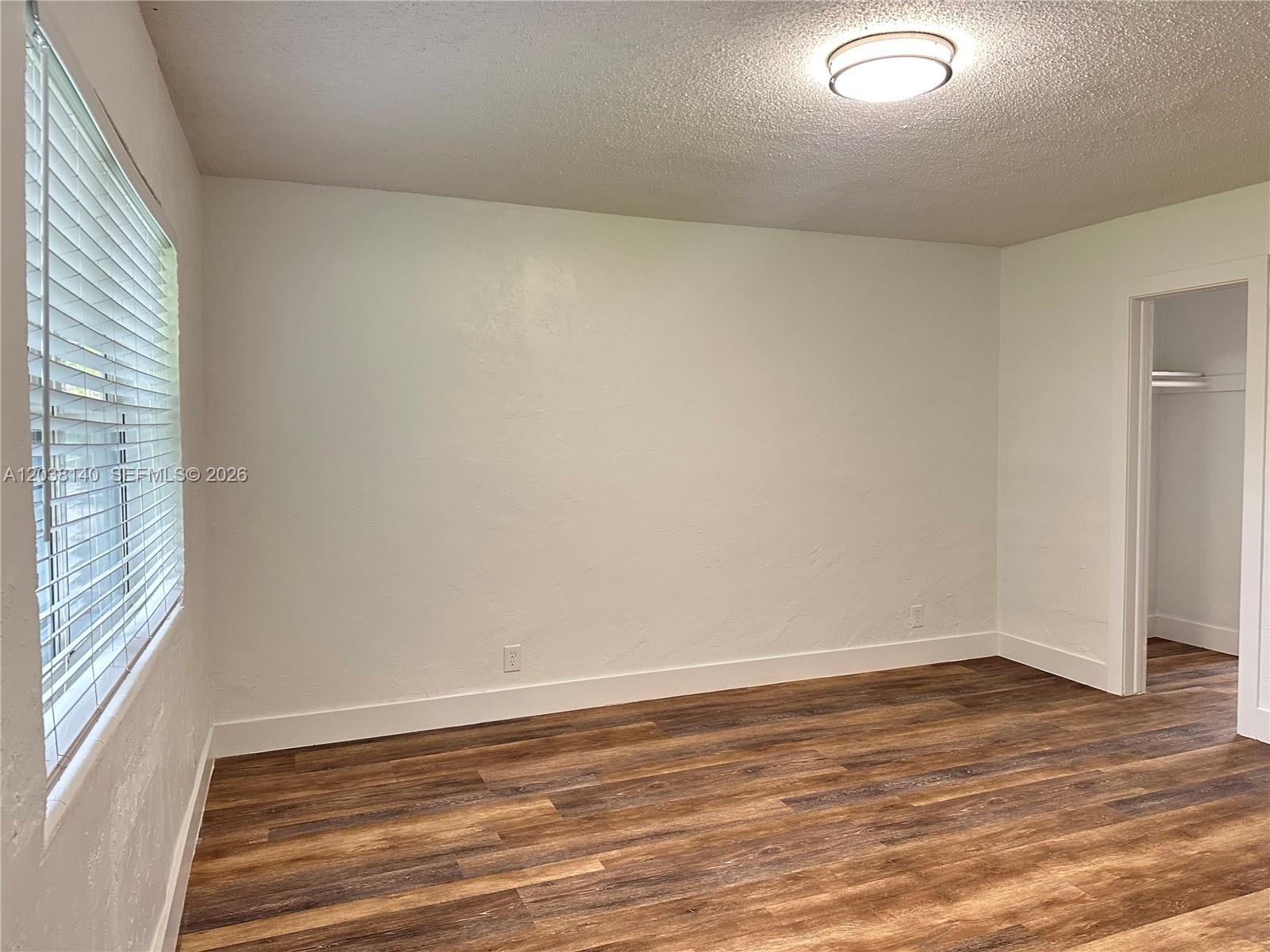 A room with wood-look flooring leads to a small kitchen with white appliances and cabinets — 1821 Thomas St # 2, Hollywood FL 33020, HOLLYWOOD, FL