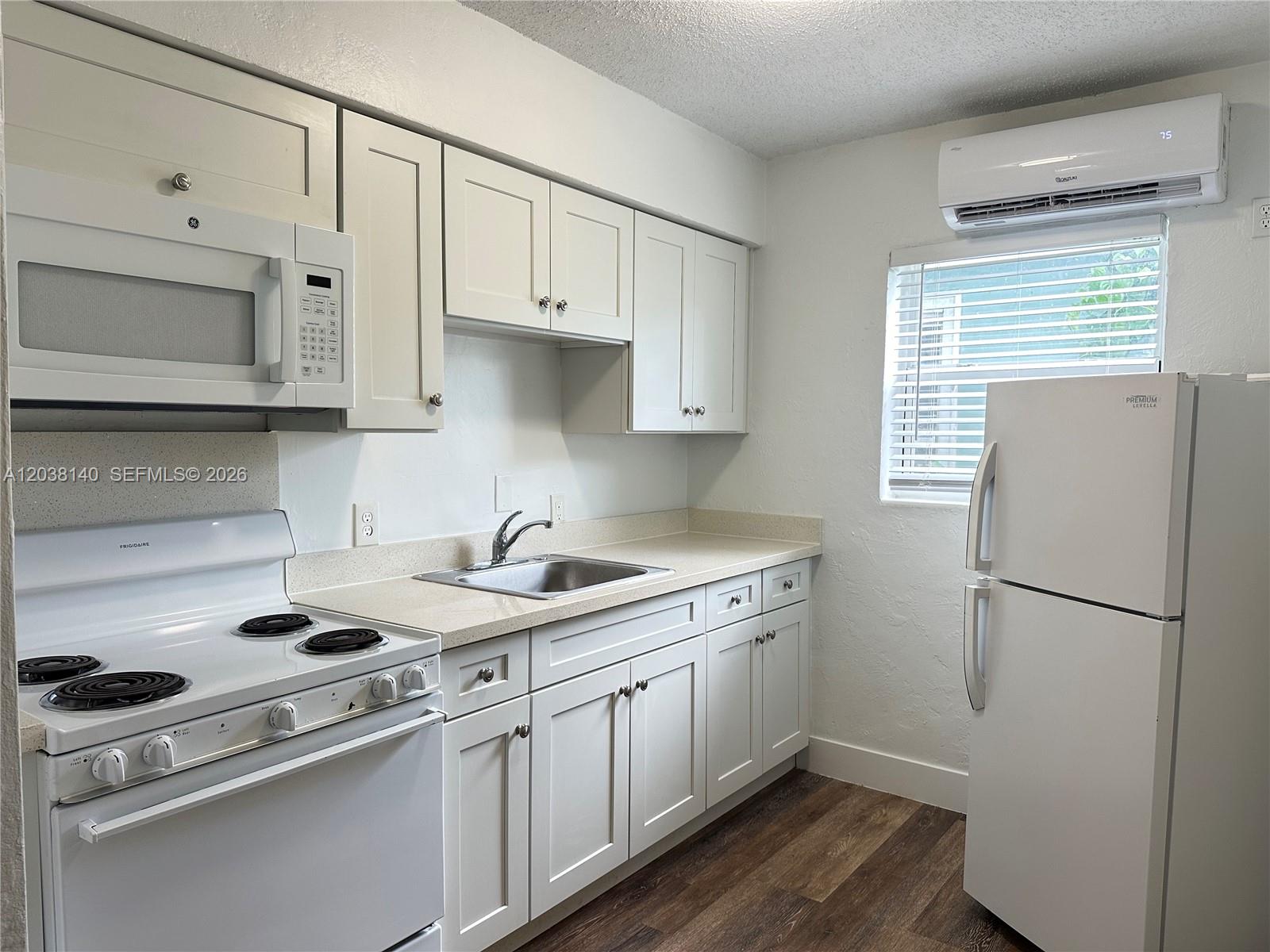 A kitchen with a white stove and microwave overlooks a living area with wood flooring — 1821 Thomas St # 2, Hollywood FL 33020, HOLLYWOOD, FL