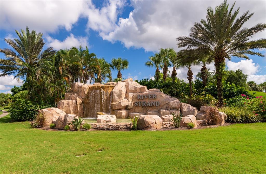 A stone waterfall monument with the text River Strand sits in a landscaped grassy area — 6515 GRAND ESTUARY TRAIL UNIT 107, BRADENTON, FL