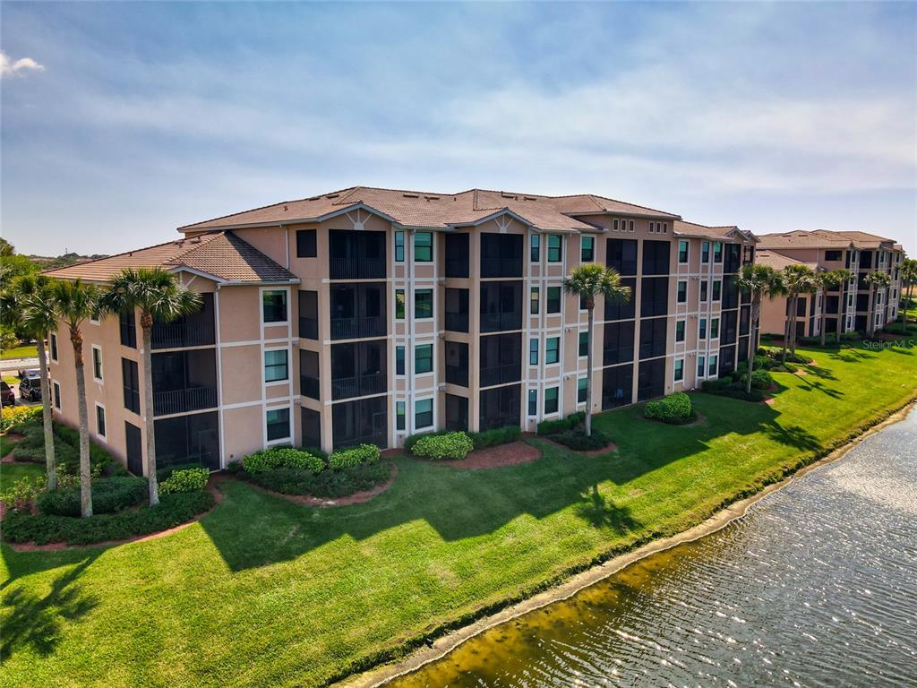An aerial view of a multi-story tan apartment building situated next to a pond — 6515 GRAND ESTUARY TRAIL UNIT 107, BRADENTON, FL