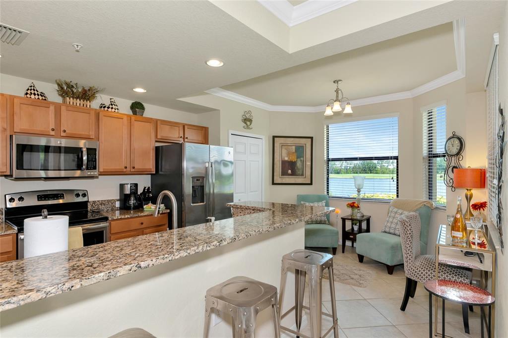 A kitchen with granite countertops, wooden cabinets, and a breakfast nook overlooking a lake — 6515 GRAND ESTUARY TRAIL UNIT 107, BRADENTON, FL