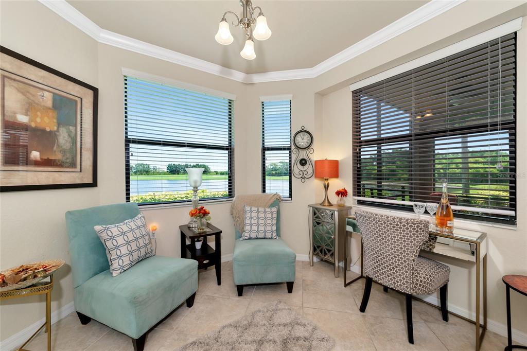 A sunroom with two teal chairs, a desk, and large windows overlooking a lake — 6515 GRAND ESTUARY TRAIL UNIT 107, BRADENTON, FL