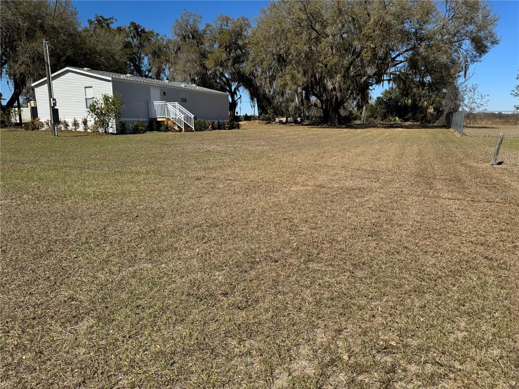 A light-colored manufactured home sits on a large, grassy lot with mature trees — 5525 W EVANS STREET, COLEMAN, FL