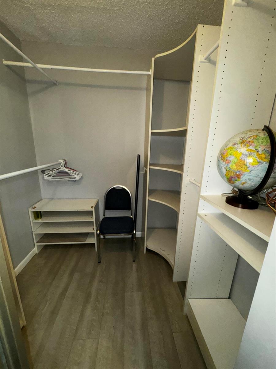 A walk-in closet features white shelving, a hanging rod, a chair, and wood-look flooring — 1908 Players Place, North Lauderdale FL 33068, NORTH LAUDERDALE, FL