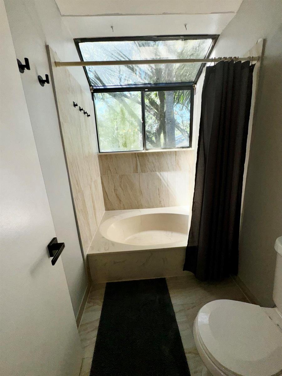 A bathroom features a tiled soaking tub under a large window with a shower curtain — 1908 Players Place, North Lauderdale FL 33068, NORTH LAUDERDALE, FL