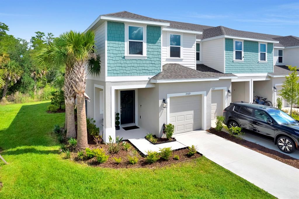A two-story townhouse with teal shingle siding, a garage, and a palm tree in front — 3569 MAYFAIR STREET, KISSIMMEE, FL