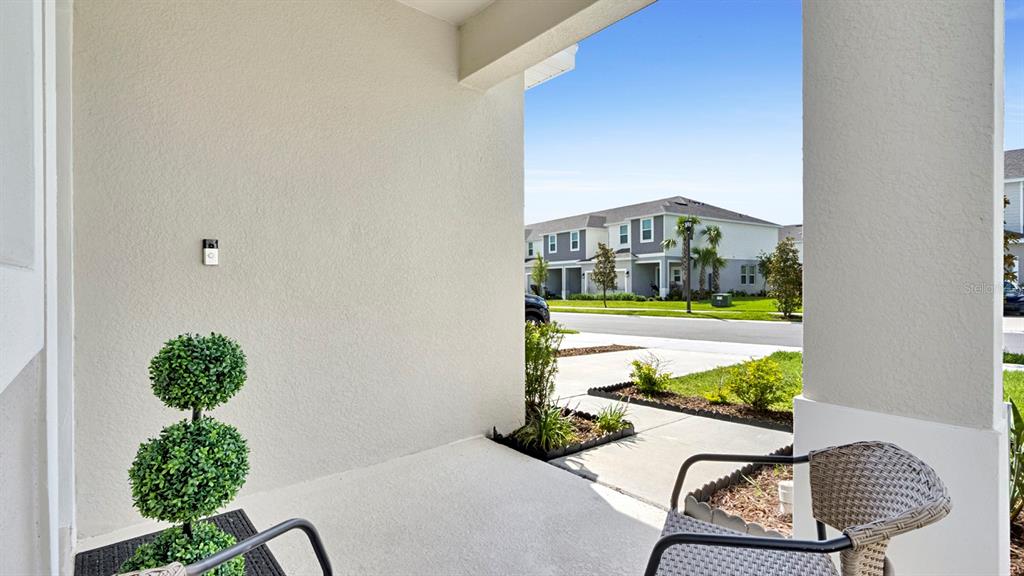 A covered entryway features a textured wall, a small topiary, and a wicker chair — 3569 MAYFAIR STREET, KISSIMMEE, FL
