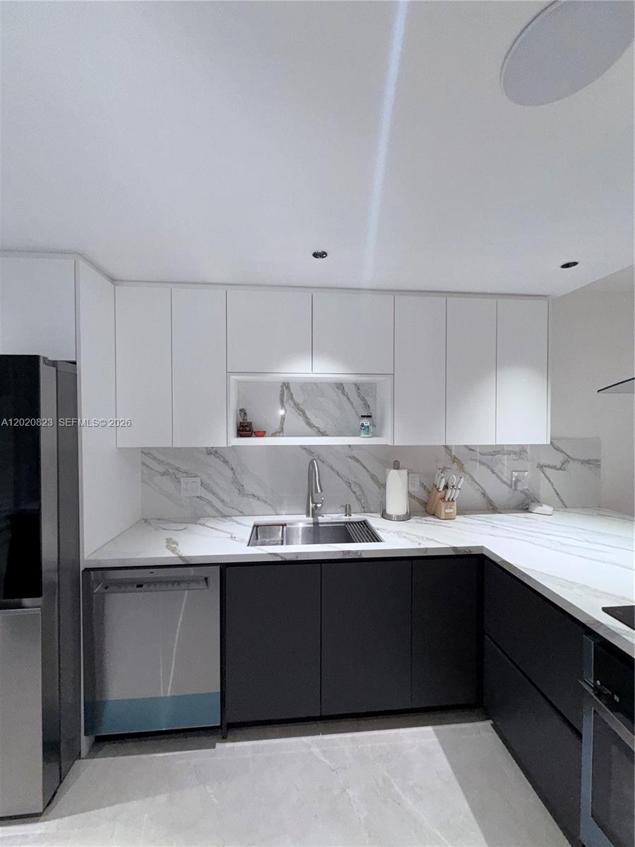 A modern kitchen features white upper cabinets, dark lower cabinets, and marble-patterned countertops and backsplash — 605 Oaks Dr # 307, Pompano Beach FL 33069, POMPANO BEACH, FL
