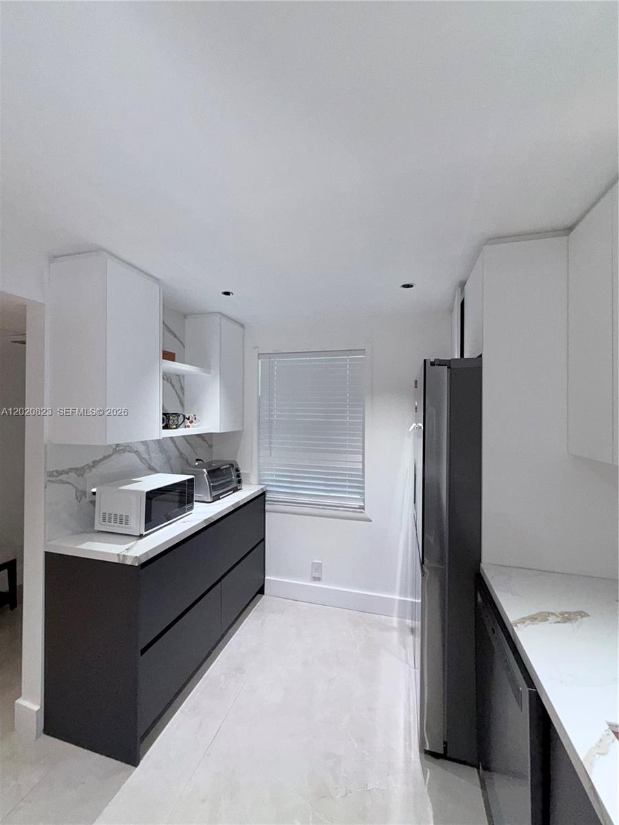 A modern kitchen features dark lower cabinets, white upper cabinets, and white marble-patterned countertops — 605 Oaks Dr # 307, Pompano Beach FL 33069, POMPANO BEACH, FL