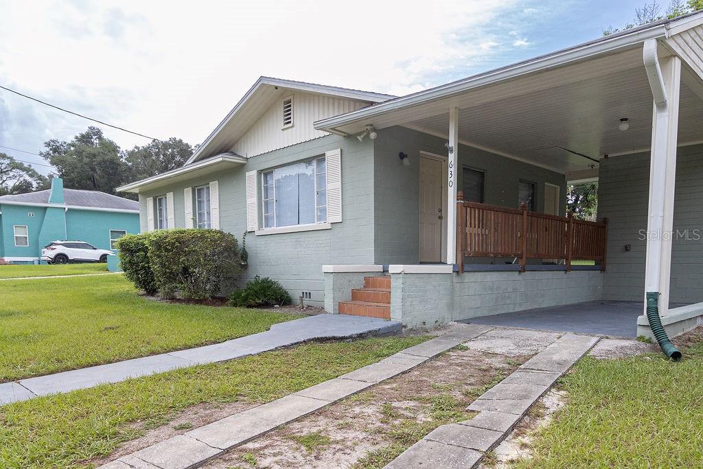 A light green single-story house with a carport, front porch, and concrete driveway — 630 E INDIANA AVENUE, DELAND, FL
