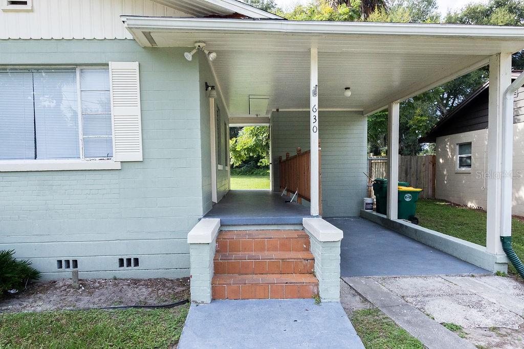 A light green house exterior features a covered porch with brick steps and a carport — 630 E INDIANA AVENUE, DELAND, FL