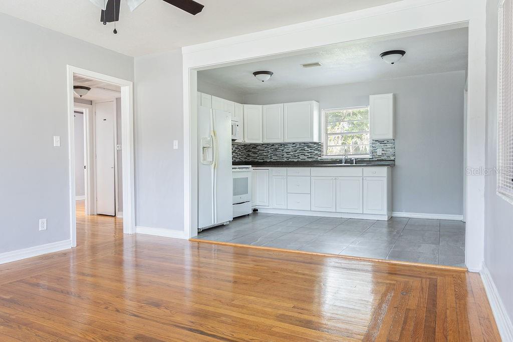 A kitchen with white cabinets and gray tile flooring opens into a hardwood-floored living area — 630 E INDIANA AVENUE, DELAND, FL