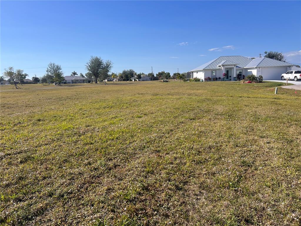 A large, grassy vacant lot sits in front of a modern suburban house — 25325 LYCHEE COURT, PUNTA GORDA, FL