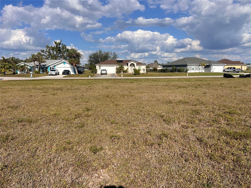 A vacant, grassy lot sits in front of several suburban houses under a cloudy sky — 25325 LYCHEE COURT, PUNTA GORDA, FL