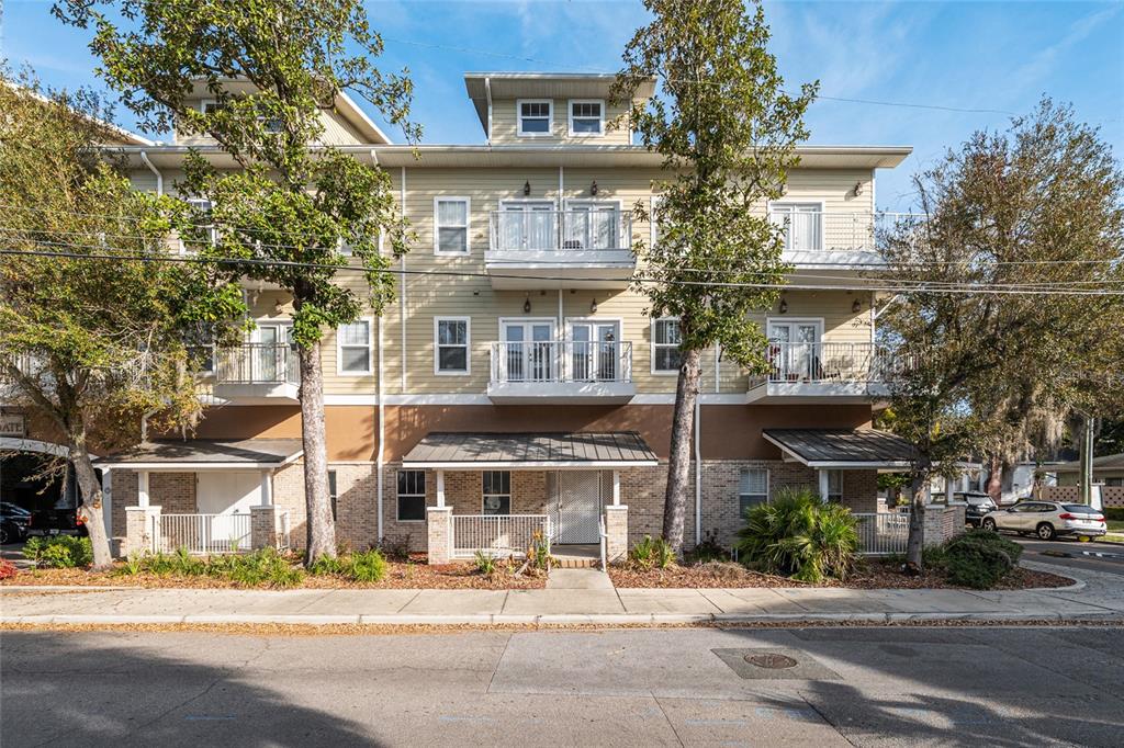 A three-story apartment building with beige siding, brick lower levels, and multiple balconies — 1500 NW 4TH AVENUE UNIT 203, GAINESVILLE, FL
