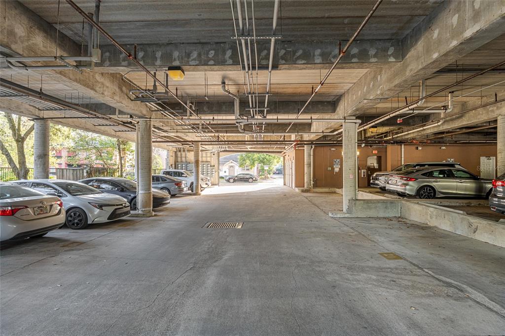 A covered concrete parking garage with multiple parked cars and exposed overhead pipes — 1500 NW 4TH AVENUE UNIT 203, GAINESVILLE, FL