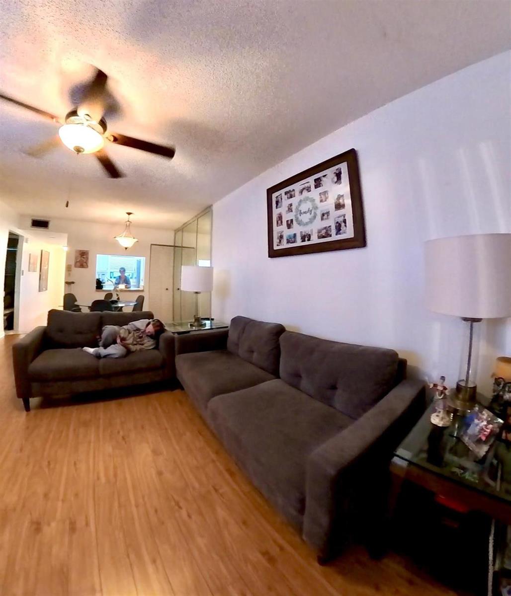 A living room features two gray sofas, wood-look flooring, and a framed family photo collage — 2161 W Woolbright Road # m202, Boynton Beach FL 33426, BOYNTON BEACH, FL