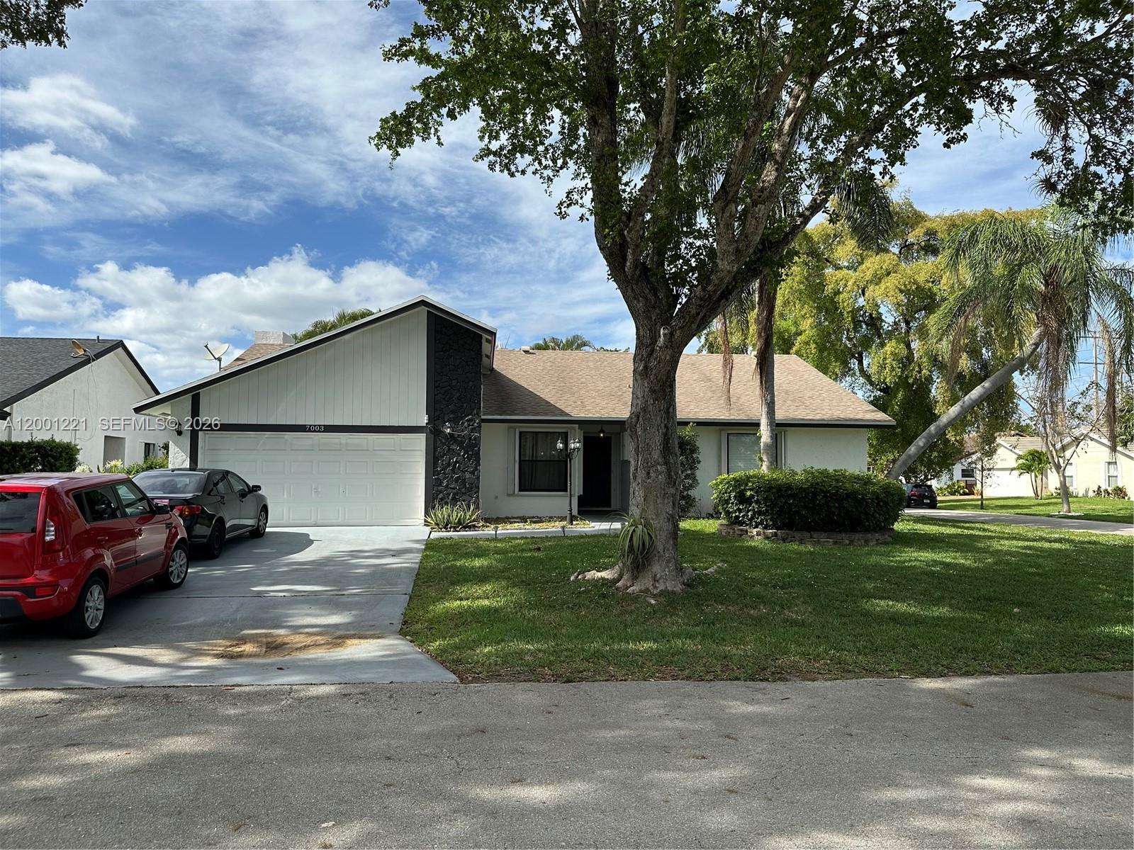 A single-story house with a white exterior, a black stone accent wall, and a large tree — 7003 NW 40th Pl, Coral Springs FL 33065, CORAL SPRINGS, FL