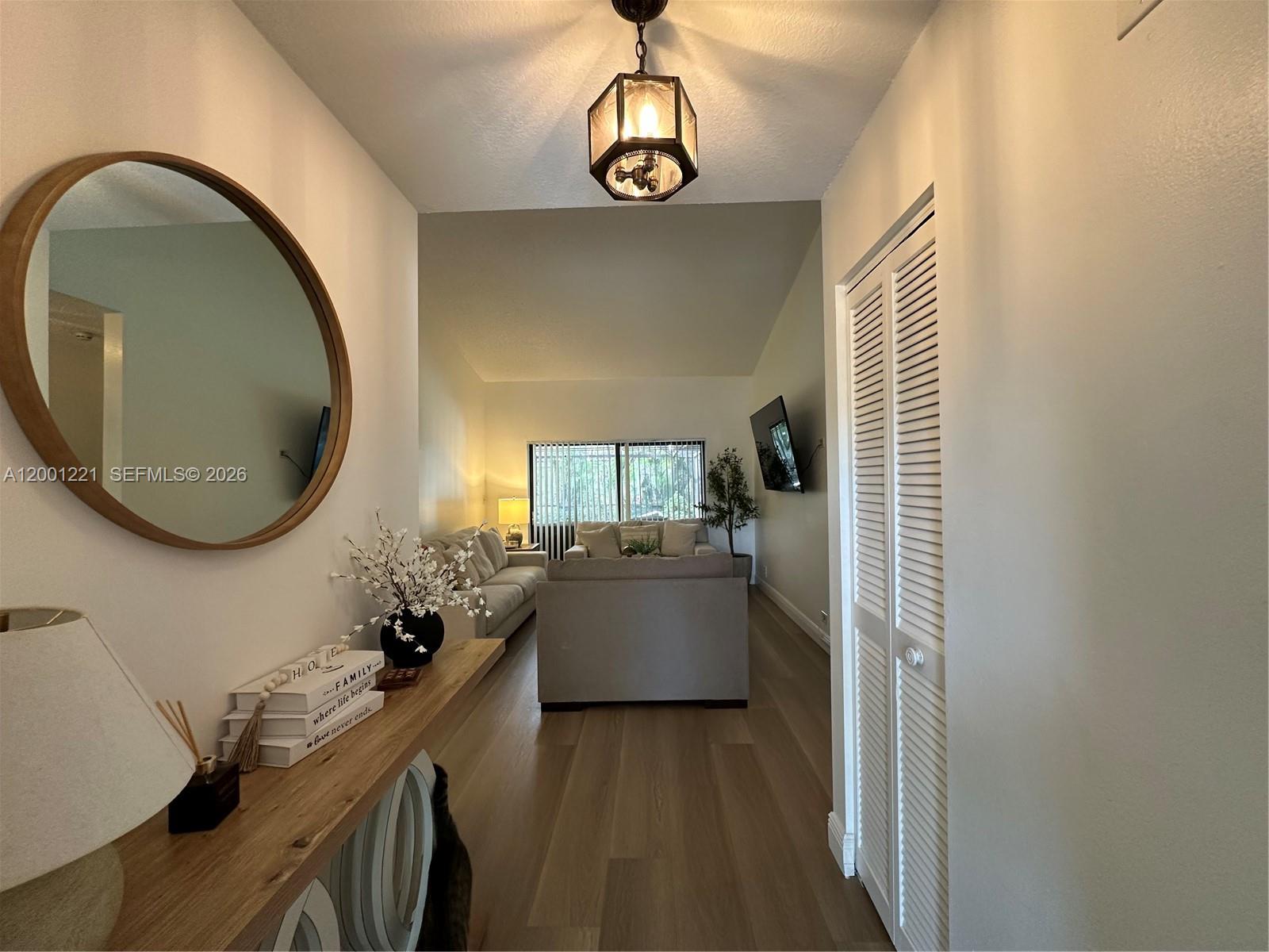 A hallway with a round mirror and console table leads into a living room area — 7003 NW 40th Pl, Coral Springs FL 33065, CORAL SPRINGS, FL
