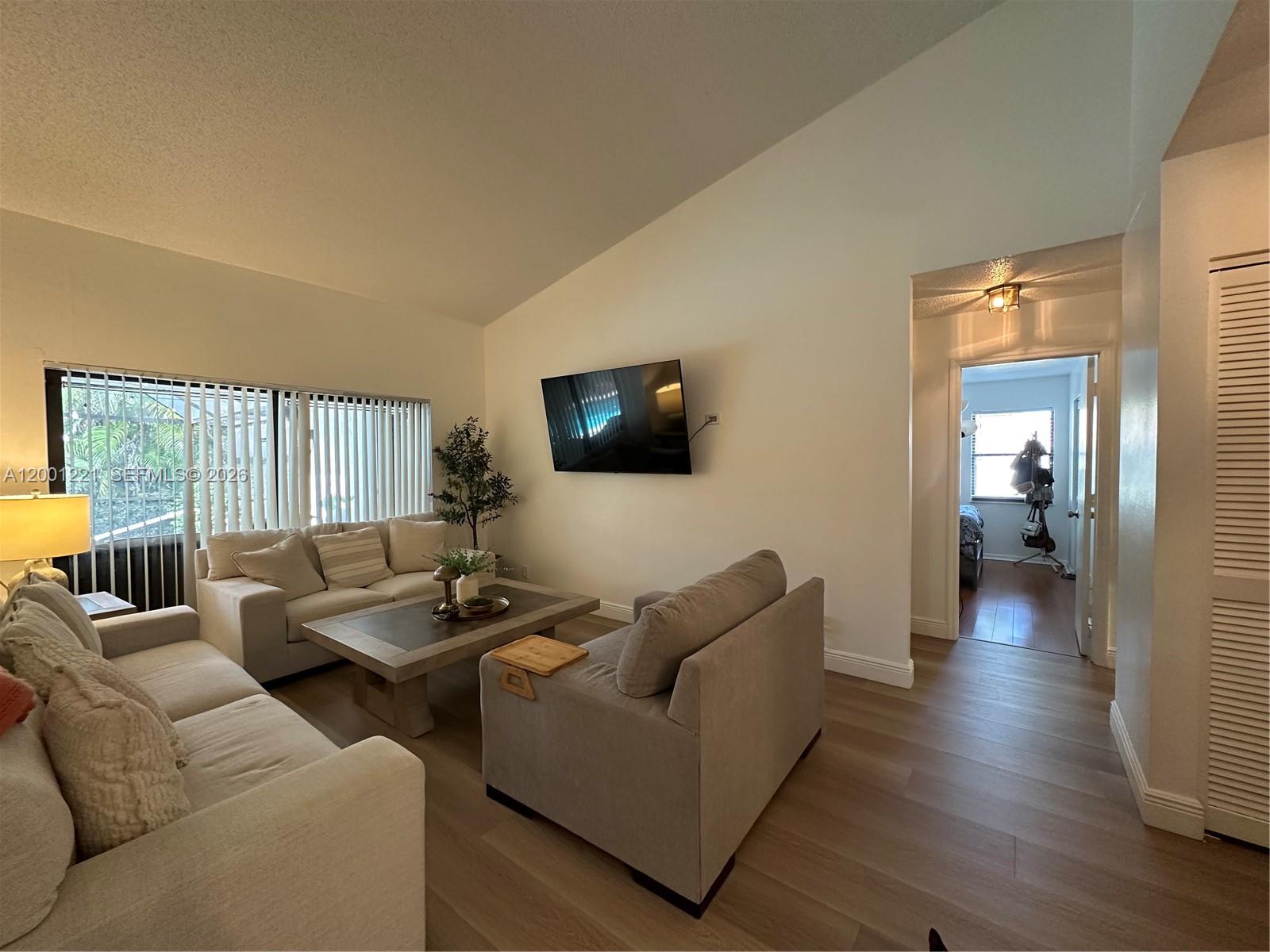 A living room features light-colored sofas, a coffee table, a wall-mounted television, and wood flooring — 7003 NW 40th Pl, Coral Springs FL 33065, CORAL SPRINGS, FL