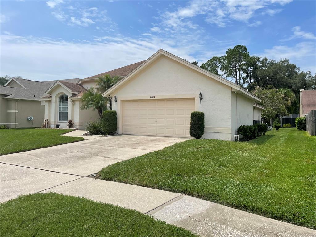 A single-story house with a beige stucco exterior, a two-car garage, and a concrete driveway — 28719 RALEIGH PLACE, WESLEY CHAPEL, FL