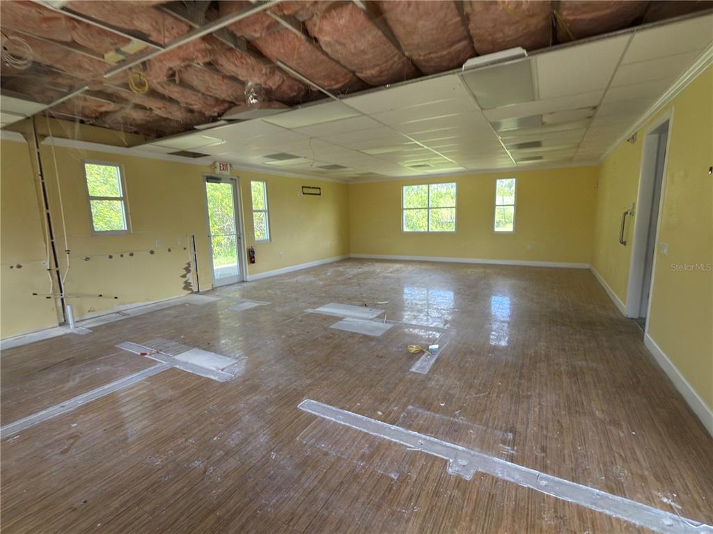 An unfinished commercial space features yellow walls, wood-look flooring, and an exposed ceiling with insulation — 3075 BOBCAT VILLAGE CENTER ROAD, NORTH PORT, FL