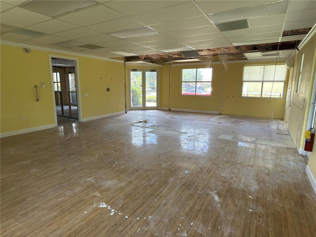 An interior view of a vacant commercial space with yellow walls, wood-look flooring, and damaged ceilings — 3075 BOBCAT VILLAGE CENTER ROAD, NORTH PORT, FL