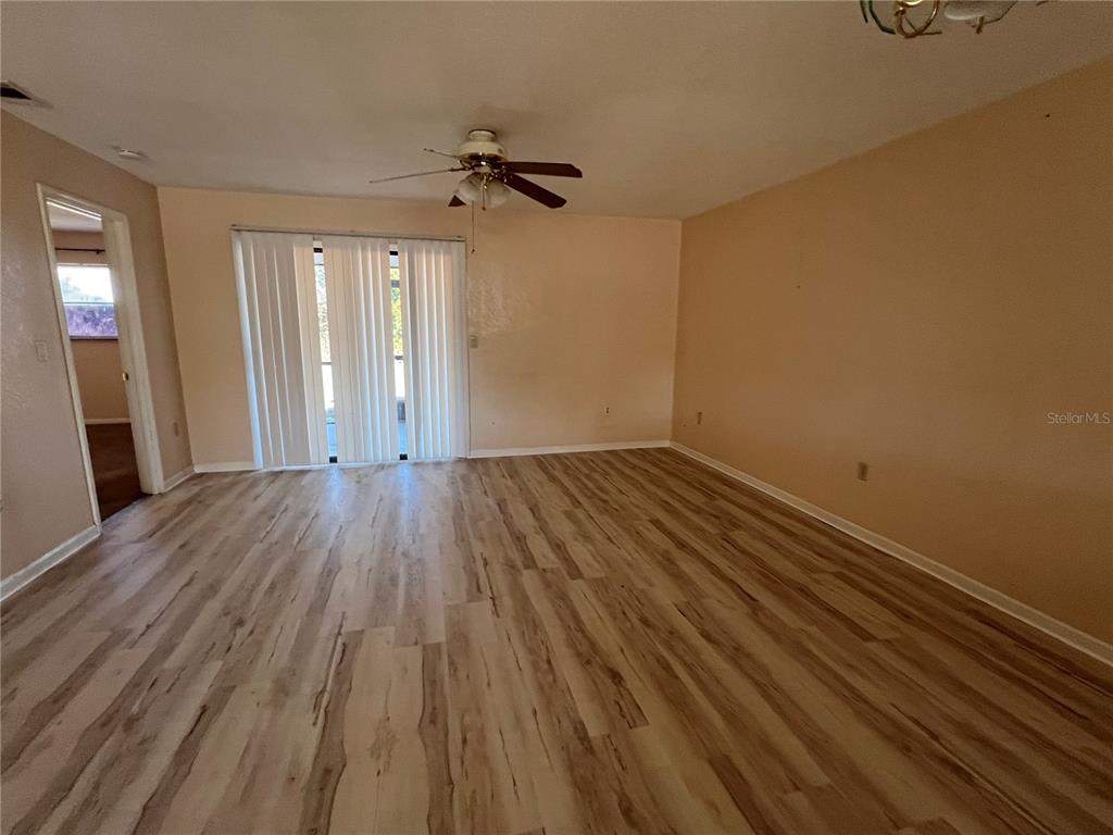 An empty living room features light wood-look flooring, beige walls, and a ceiling fan — 27082 ADAMS STREET UNIT A, PUNTA GORDA, FL