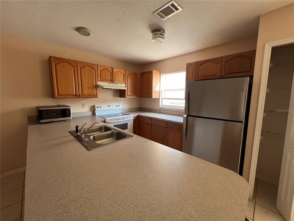 A kitchen features wood cabinets, laminate countertops, a stainless steel refrigerator, and a double sink — 27082 ADAMS STREET UNIT A, PUNTA GORDA, FL