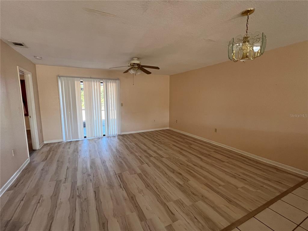 An empty living room features light wood-look flooring, a ceiling fan, and sliding glass doors — 27082 ADAMS STREET UNIT A, PUNTA GORDA, FL