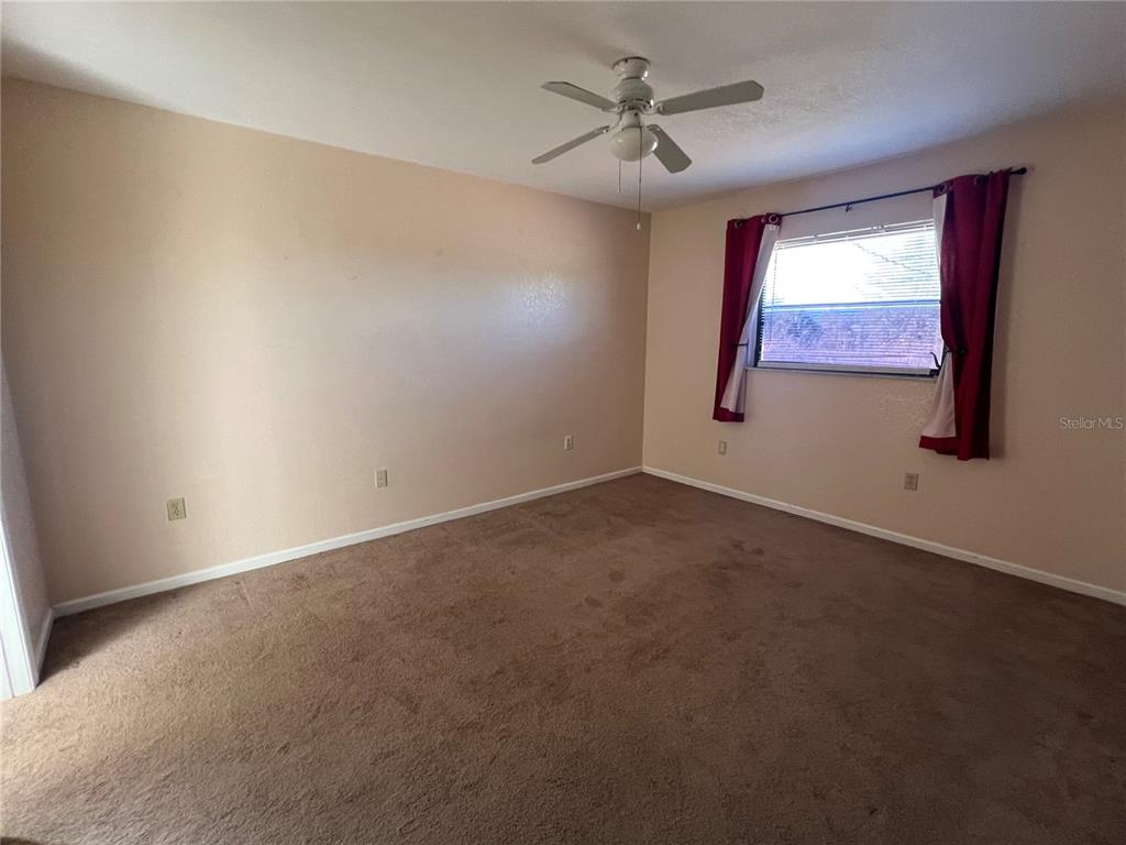 An empty bedroom features beige walls, brown carpeting, a ceiling fan, and a window with curtains — 27082 ADAMS STREET UNIT A, PUNTA GORDA, FL