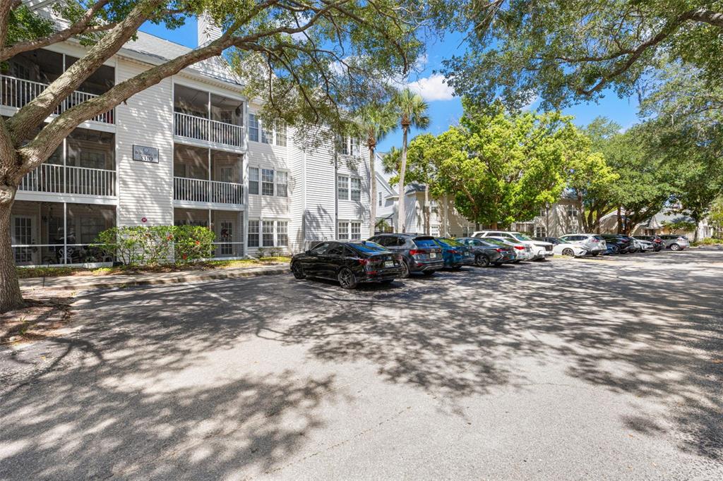 A multi-story apartment building with screened balconies sits next to a paved parking lot — 3310 HAVILAND COURT UNIT 104, PALM HARBOR, FL