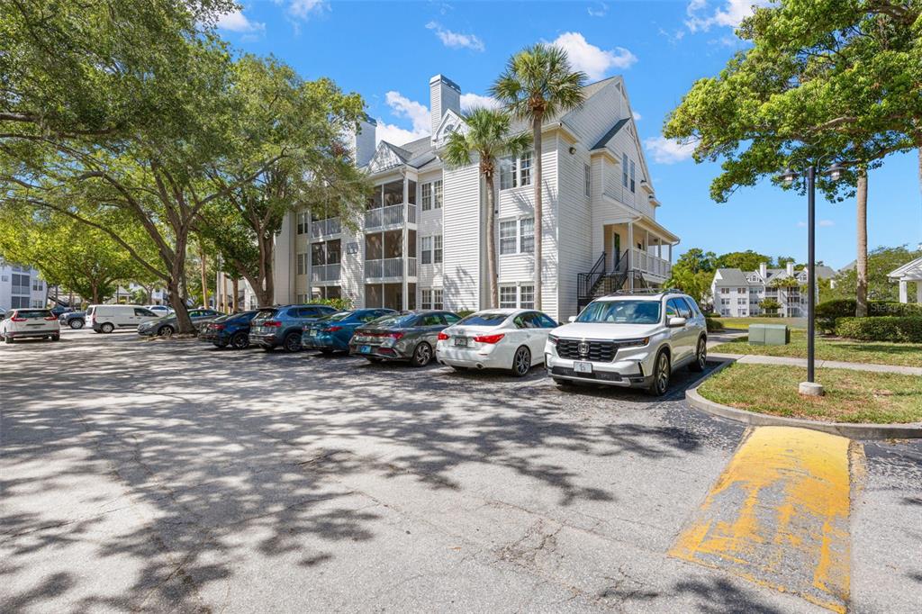 A multi-story apartment building with a parking lot and several parked cars in front — 3310 HAVILAND COURT UNIT 104, PALM HARBOR, FL