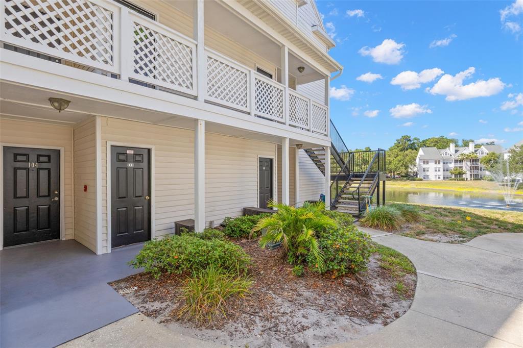 The exterior of a multi-story apartment building features a walkway, stairs, and a pond — 3310 HAVILAND COURT UNIT 104, PALM HARBOR, FL