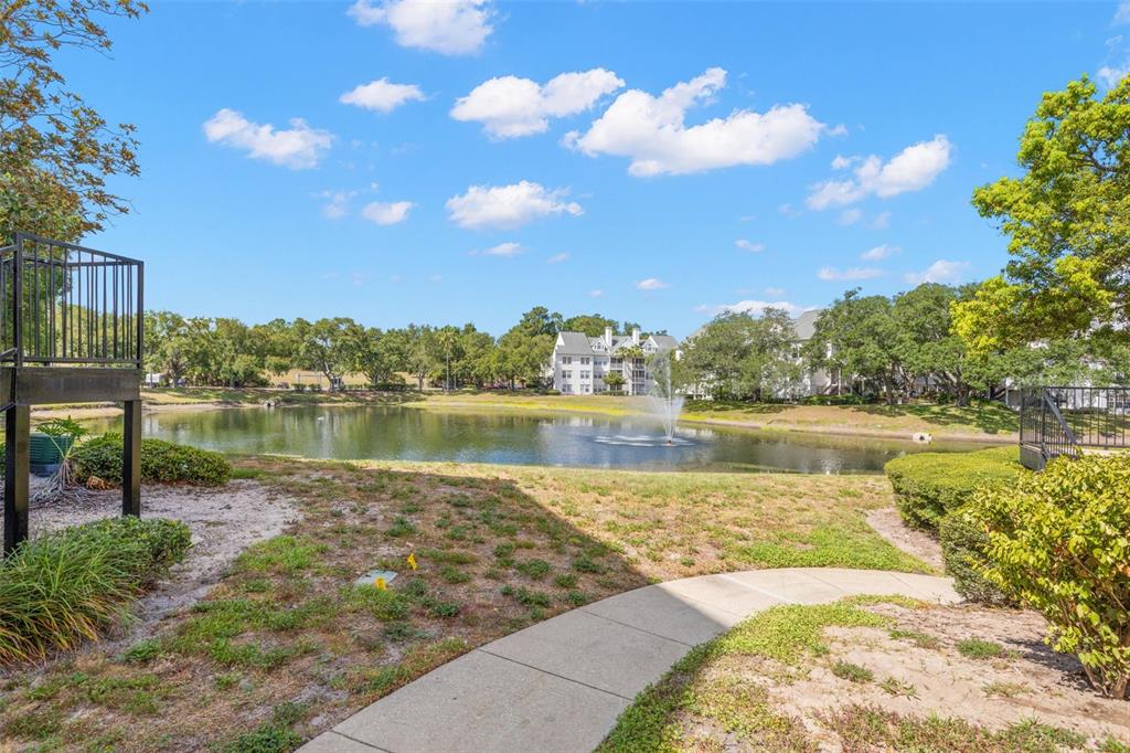 A view of a pond with a fountain, surrounded by trees and apartment buildings — 3310 HAVILAND COURT UNIT 104, PALM HARBOR, FL
