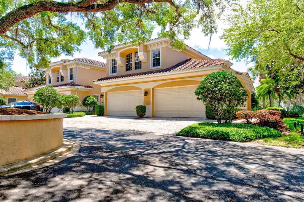 A two-story house with a two-car garage and a paved driveway under large oak trees — 54 CAMINO REAL BOULEVARD UNIT 504, HOWEY IN THE HILLS, FL