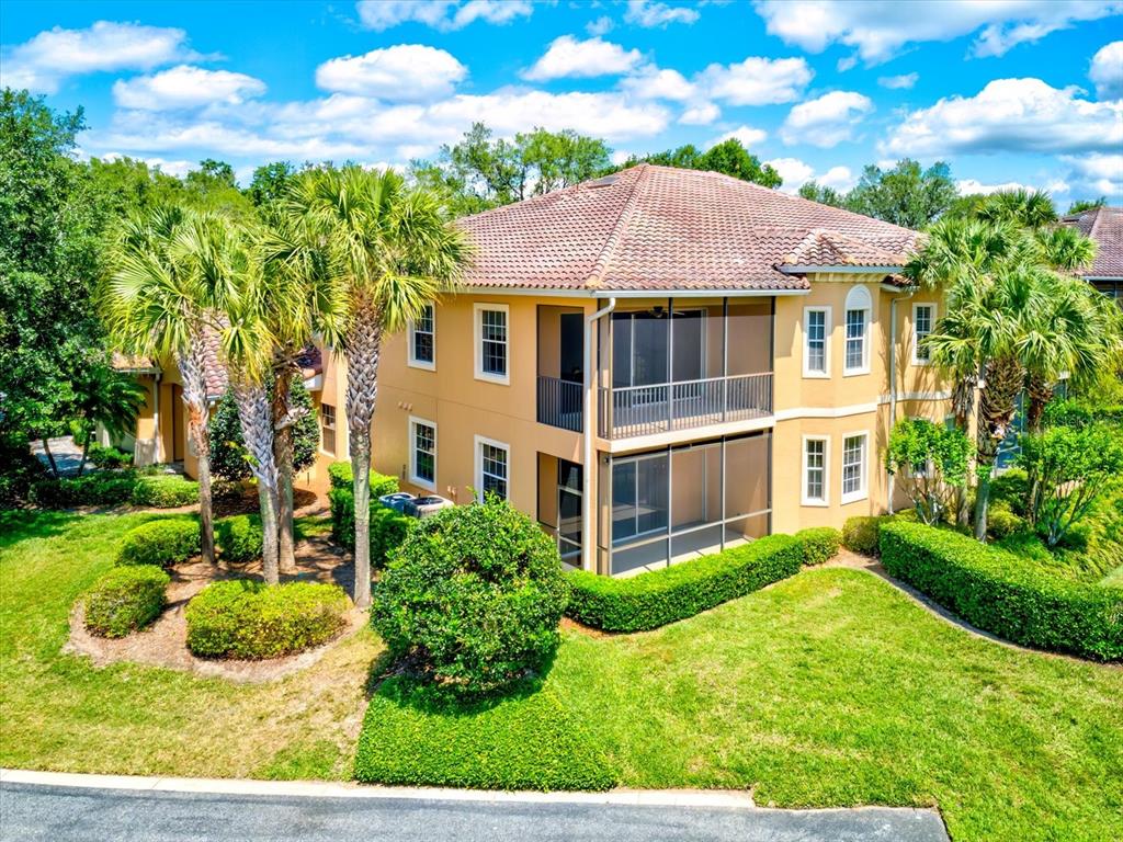 A two-story tan stucco building features a tiled roof and screened-in balconies — 54 CAMINO REAL BOULEVARD UNIT 504, HOWEY IN THE HILLS, FL